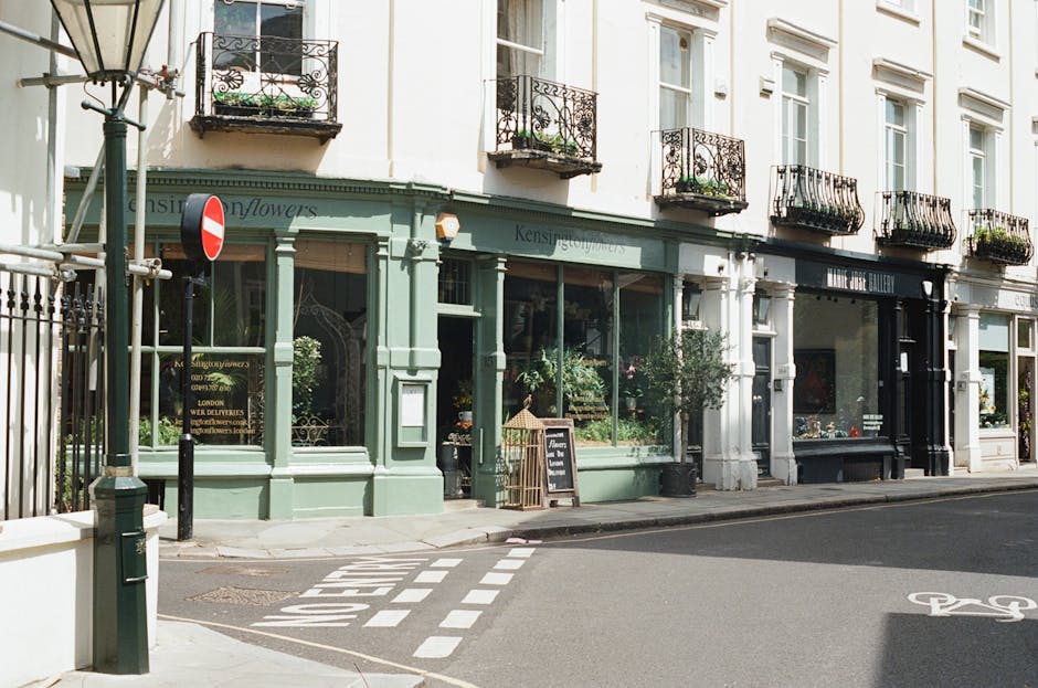 A glimpse of a charming florist shop on Chelsea Bridge Road, featuring a light green facade with large display windows showcasing fresh flowers and floral arrangements inside. The shop has black wroug