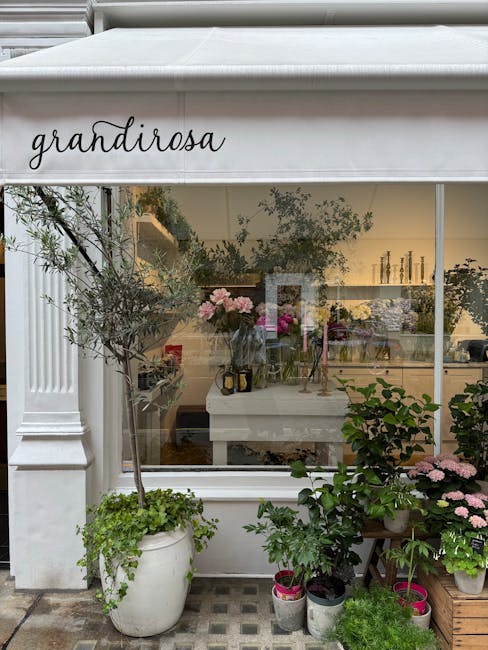The image shows the exterior of a florist shop called 'Grandirosa' with a white awning displaying the shop name in elegant black script. Through the large glass window, a floral display is visible ins